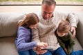 Grandchildren On Sofa At Home Showing Grandfather How To Use Mobile Phone