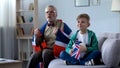 Granddad wrapped in British flag watching soccer with boy, worrying about game Royalty Free Stock Photo