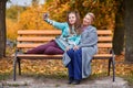 Granddaughter and grandmother do selfie on a bench in an autumn park