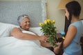 Granddaughter giving flowers to grandmother in bed room Royalty Free Stock Photo