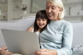 Granddaughter and grandma using laptop sitting on couch at home Royalty Free Stock Photo