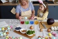 Granddaughter with grandmother dyeing Easter eggs on the table