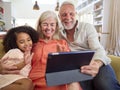 Granddaughter And Grandparents On Sofa At Home Making Video Call On Digital Tablet Royalty Free Stock Photo