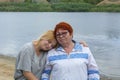 Granddaughter hugs her grandmother by the river in summer. The concept of family and friendship of different generations. Soft