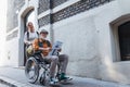 Granddaughter pushing senior man in wheelchair on street. Buying newspaper in newsstand. Female caregiver and elderly Royalty Free Stock Photo