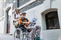 Granddaughter pushing senior man in wheelchair on street. Buying newspaper in newsstand. Female caregiver and elderly Royalty Free Stock Photo