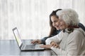 Granddaughter teaching her grandmother to use a computer on a wooden table with a colorful handkerchief