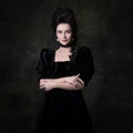 Classic retro portrait of young beautiful woman in image of medieval royal person in black dress isolated on dark