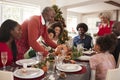 Grandfather bringing the roast turkey to the dinner table during a multi generation, mixed race family Christmas celebration, clos