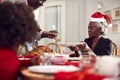 Grandfather Carving And Serving As Multi Generation Family Enjoy Eating Christmas Meal At Home