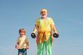 Grandfather and child lifting dumbbell. Portrait of a healthy father and son working out with dumbbells over blue sky