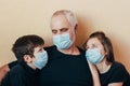 Grandfather and grandchildren in face masks sit hugging sadly thinking about restrictions imposed due to coronavirus pandemic. Fam