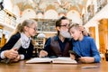 Grandfather and grandchildren sitting at the table in library and reading book. Granddad is happy, loves so much his Royalty Free Stock Photo