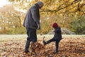 Grandfather And Granddaughter Kicking Leaves On Autumn Walk