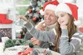 Grandfather with granddaughter in Santa hats preparing for Christmas at home