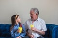 Grandfather and granddaughter sit on the sofa and drink