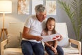 Grandfather and granddaughter sitting on couch reading handmade greeting card with red drawn heart while sitting together on sofa Royalty Free Stock Photo