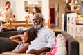 Grandfather With Granddaughter Sitting On Sofa At Home Watching Movie With Family In Background Royalty Free Stock Photo