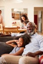 Grandfather With Granddaughter Sitting On Sofa At Home Watching Movie With Family In Background Royalty Free Stock Photo