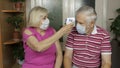 Grandfather and grandmother measures temperature with non-contact infrared thermometer. Coronavirus