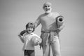 Grandfather and grandson with basketball ball and yoga mat in hands. Senior man and cute little boy exercising on blue Royalty Free Stock Photo