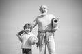 Grandfather and grandson with basketball ball and yoga mat in hands. Senior man and cute little boy exercising on blue Royalty Free Stock Photo