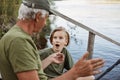 Grandfather and grandson fishing on river berth, senior man showing size of fish he caught last time, male child posing with Royalty Free Stock Photo