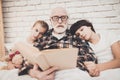 Grandfather, grandson and granddaughter at home. Grandpa and children are reading book. Royalty Free Stock Photo