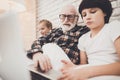 Grandfather, grandson and granddaughter at home. Grandpa and children are reading book and using laptop. Royalty Free Stock Photo