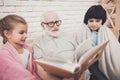 Grandfather, grandson and granddaughter at home. Grandpa and children are watching photos in album. Royalty Free Stock Photo