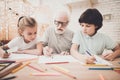 Grandfather, grandson and granddaughter at home. Children are drawing with color pencils. Royalty Free Stock Photo