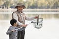 Grandfather and grandson putting fish into net at lake