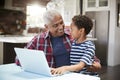 Grandfather And Grandson Sitting Around Table At Home Using Laptop Together