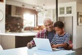 Grandfather And Grandson Sitting Around Table At Home Using Laptop Together