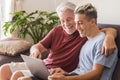 Grandfather and grandson sitting together on the sofa at home in friendship looking at the same laptop and smiling - sharing the Royalty Free Stock Photo