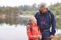 Grandfather and grandson standing on the shore of a lake looking at each other laughing, Lake District, UK