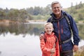 Grandfather and grandson standing together on the shore of a lake smiling to camera, close up, Lake District, UK