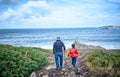 The grandfather and his grandson walk along the coast with the sea with a lot of waves breaking on the rocks Royalty Free Stock Photo