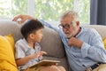 Grandfather and little cute grandson playing touchscreen tablet PC together on sofa in their house