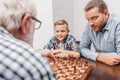 Grandfather making a move in chess game while grandson and son are Royalty Free Stock Photo