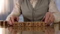 Grandfather making word hospice of wooden cubes on table, elder care, disorder