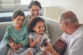 Grandfather playing the guitar for grandmother and children sitting on the sofa in their home. Retired grandparents Royalty Free Stock Photo