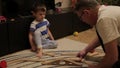 Grandfather plays with his grandson in a wooden railway on the floor. A little boy of three years with Granddaddy