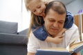 Grandfather reading a book to his little graddaughter in living room