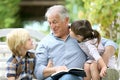 Grandfather reading story to grandchildren in the garden