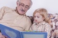 The grandfather reads a book for his grandson. The grandson listens enthusiastically to the grandfather