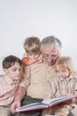 The grandfather reads a book to his grandchildren. The children listen carefully