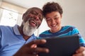 Grandfather Sitting In Chair With Grandson Watching Movie On Digital Tablet Together