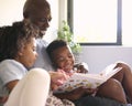 Grandfather Sitting On Sofa At Home Reading Book With Grandchildren Royalty Free Stock Photo