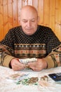 The grandfather in a sweater sits at the dacha at a table and counts money. Royalty Free Stock Photo